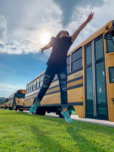 Young girl jumping next to a parked yellow school bus