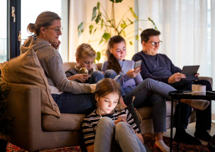 Family of five sitting on a couch, every member looking at a device